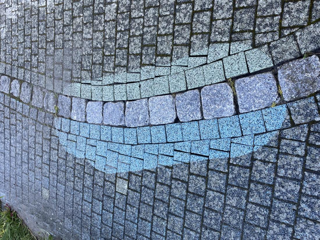 Gereinigtes Bogenelement aus blauem und violettem Pflaster, eingefasst von der noch unbehandelten Fläche, am Europaweg in Staudt