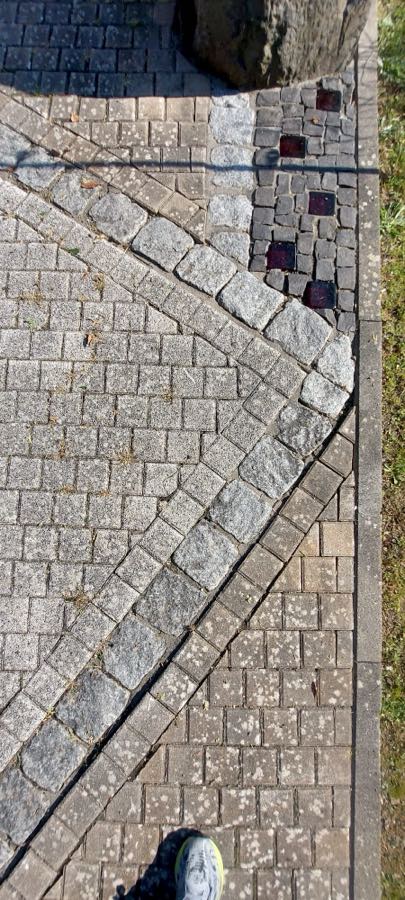 Gehwegabschnitt am Europaweg vor der Reinigung, flächig vergrünt und stumpf, am Europaweg in Staudt