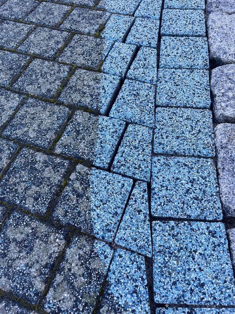 Diagonale Grenze zwischen dem gereinigten, kräftig blauen Pflaster und dem stumpfen, bemoosten Bereich, am Europaweg in Staudt