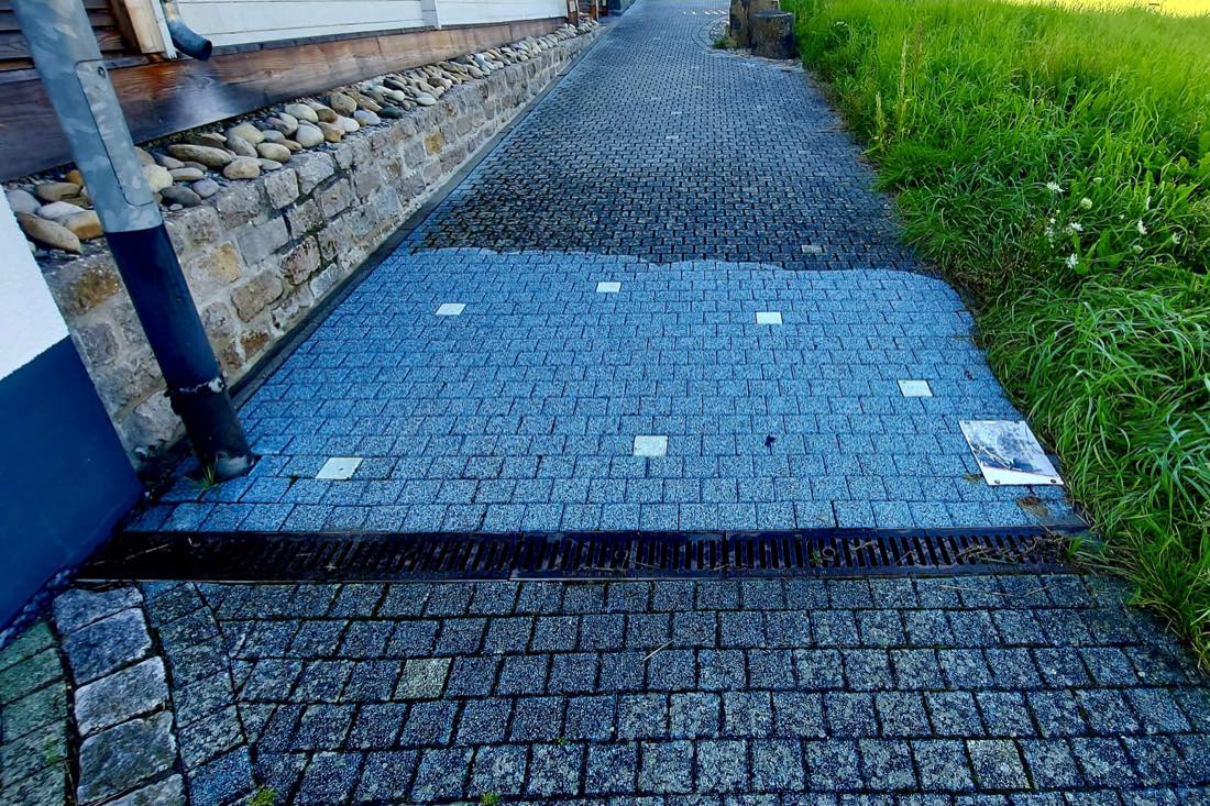 Zuwegung neben einem Wohnhaus, der gereinigte Abschnitt hebt sich deutlich vom übrigen Pflaster ab