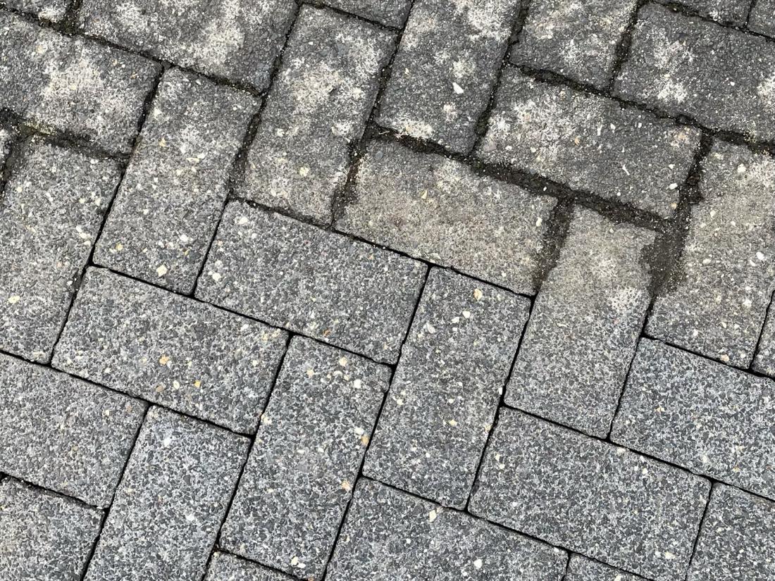 Dunkles Betonpflaster mit scharfer Trennlinie zwischen bewachsenem und gereinigtem Bereich